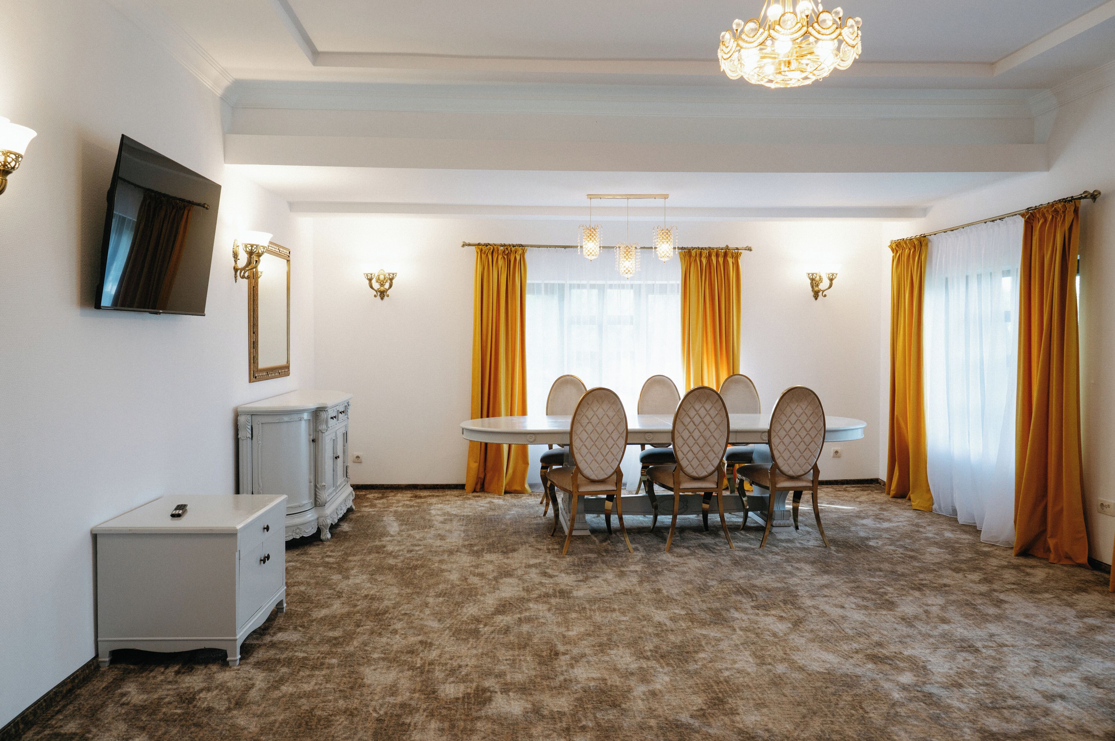 A dining area with a round table, chairs, a chandelier, and curtains.