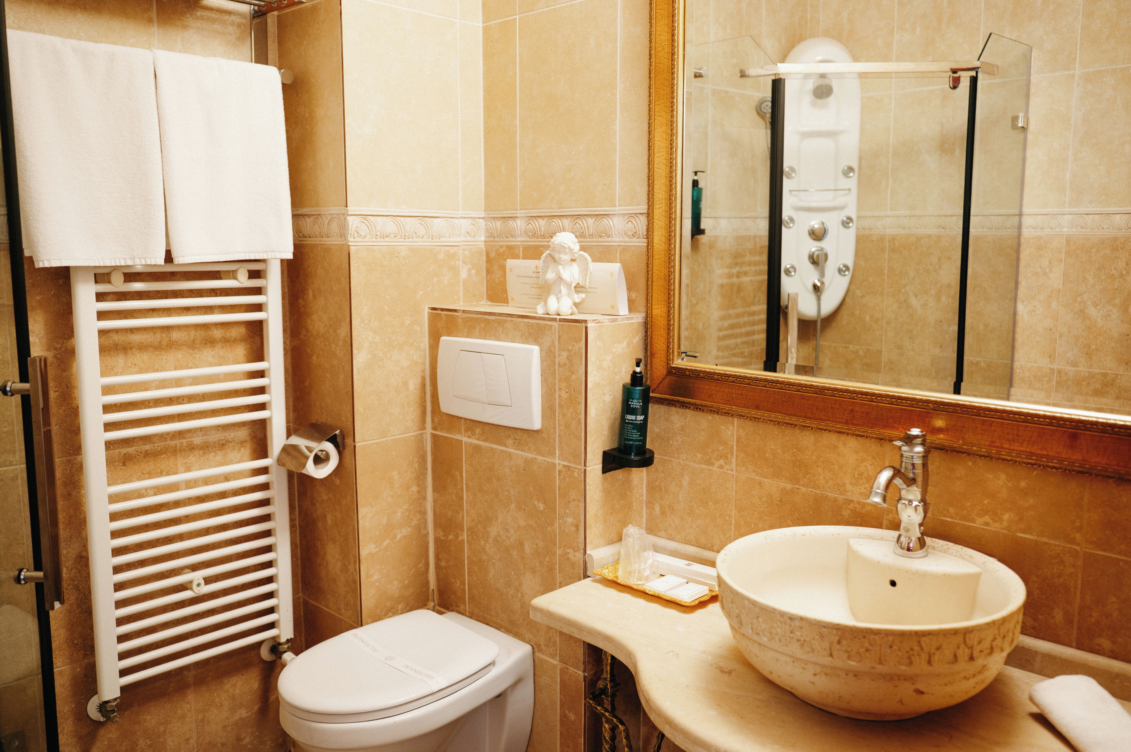 A bathroom with a toilet, a sink with a marble basin, a towel rack with towels, a mirror, and a shower area.