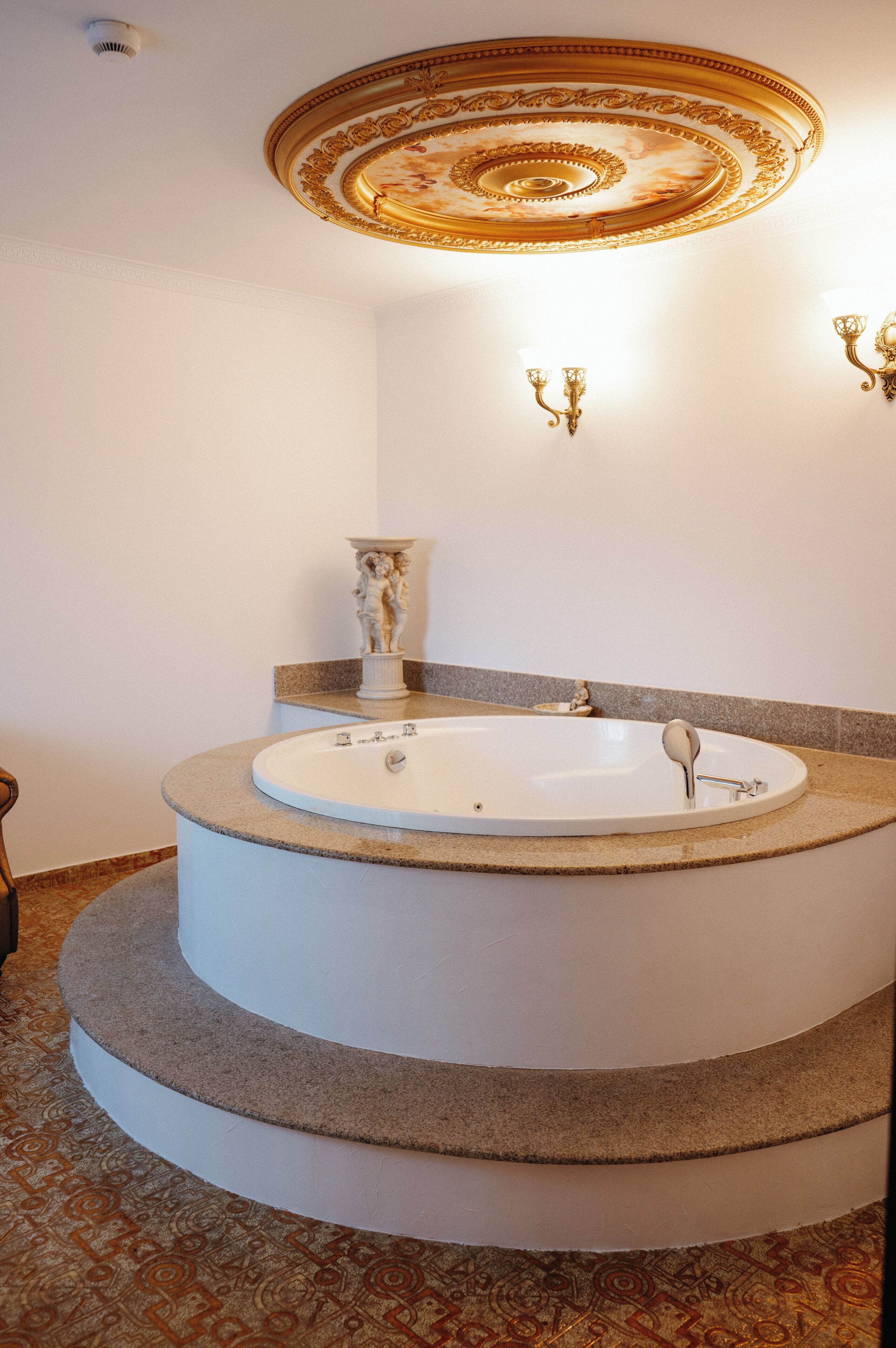 A bathroom with a freestanding bathtub, a decorative ceiling, and wall-mounted sconces.