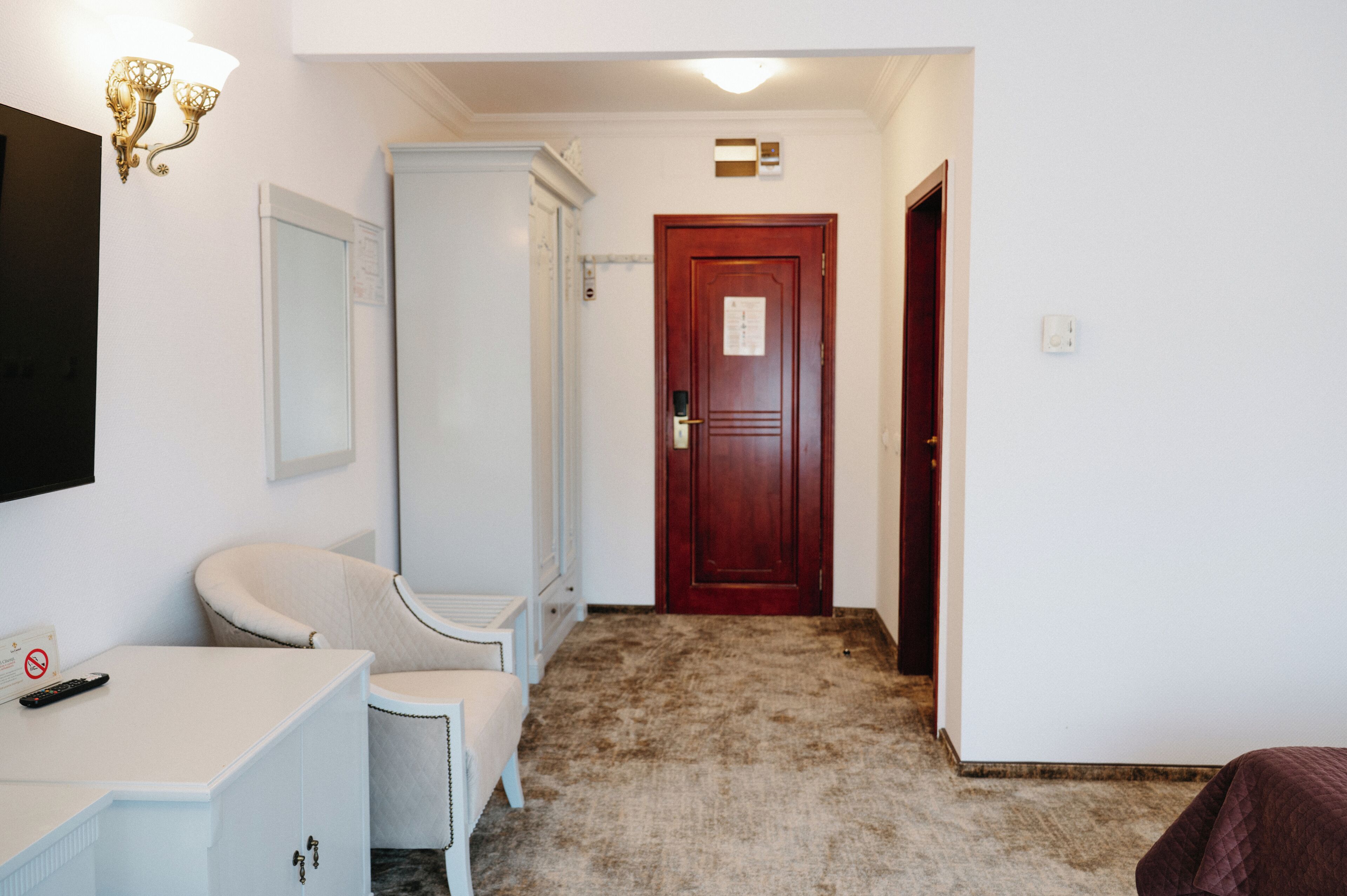 Ein Hotelzimmer mit weißem Schreibtisch, beigem Sessel, Holztür und Teppichboden.