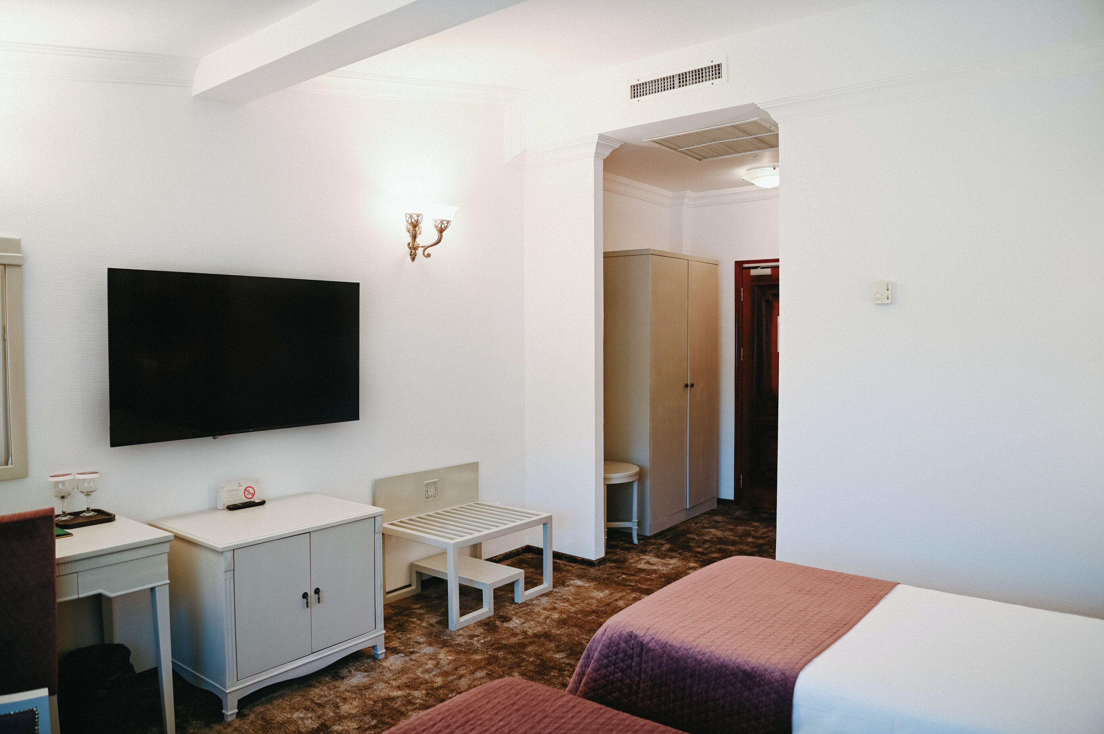 Une chambre d’hôtel comprenant un lit, un bureau avec un téléviseur à écran plat, une petite table, une armoire et une porte donnant accès à une salle de bain.