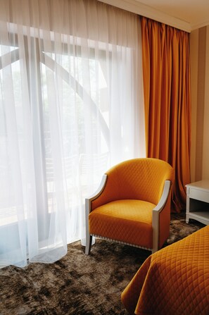 A hotel room with a large window, a single orange chair, a white nightstand, and a brown carpet. - Hotel La Castel Iasi (Iași)