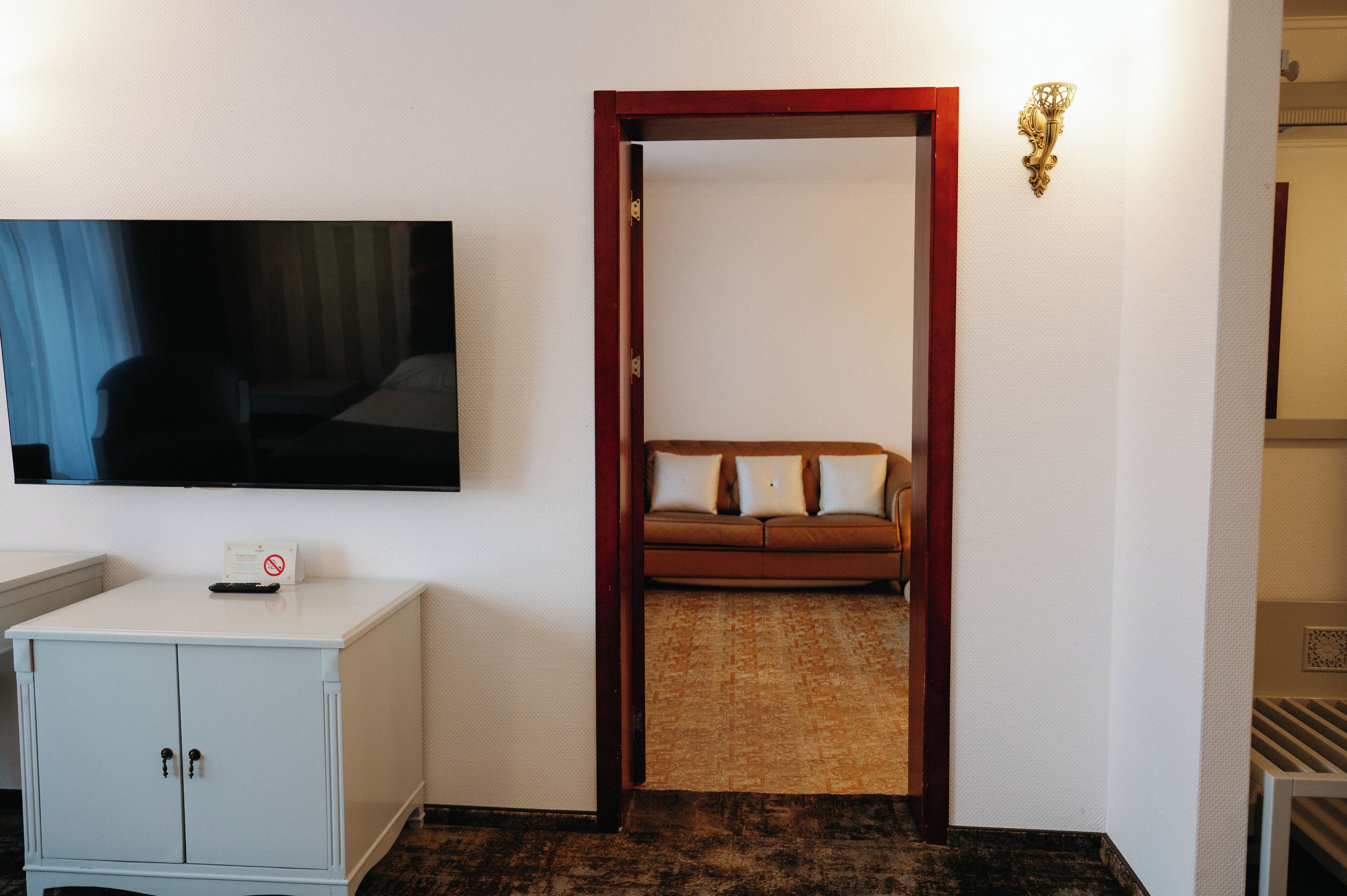 Habitación de hotel con una televisión sobre un mueble, un sofá con cojines y una puerta con una placa decorativa en la pared.