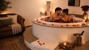 Una pareja en un jacuzzi con pétalos de rosa, velas y champán.