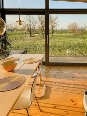 Ein Essbereich mit Tisch, Stühlen und Blick auf ein grünes Feld durch große Fenster.