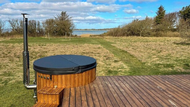 Een hottub op een houten terras, met een grasveld en bomen op de achtergrond.