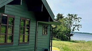 Een groene houten woning met schuin dak, een veranda en uitzicht op een waterpartij.