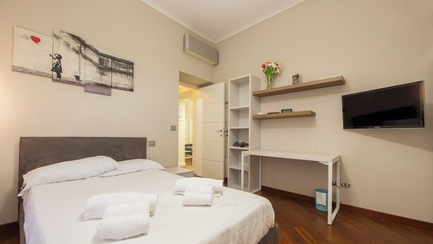 Habitación de hotel con una cama, un escritorio, un televisor y un cuadro en la pared.