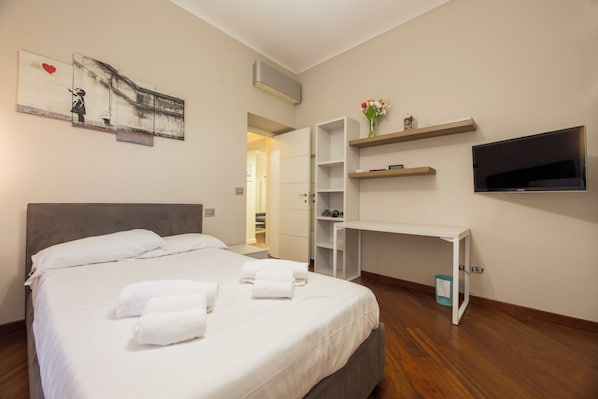 Ein Hotelzimmer mit Bett, Schreibtisch, Fernseher und einem Gemälde an der Wand.
