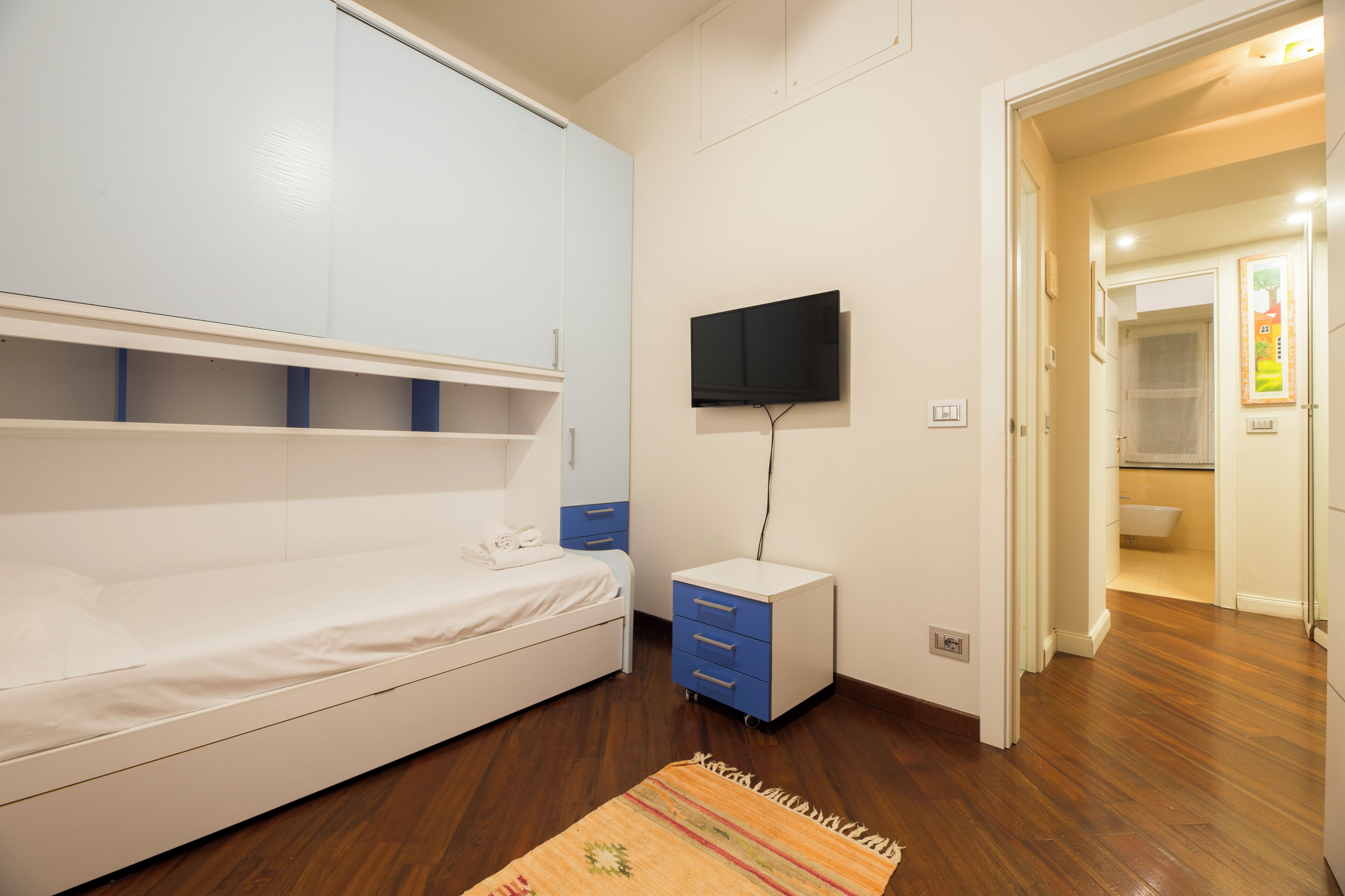A bedroom with a bed, a TV, a small bedside table, and a door leading to a bathroom.