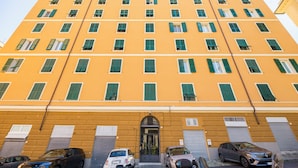 Un edificio de varios pisos con fachada amarilla, múltiples ventanas con contraventanas verdes y una entrada central.