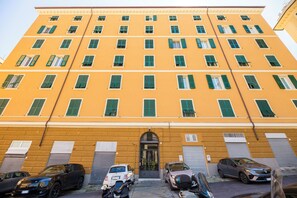 Ein mehrstöckiges Gebäude mit gelber Fassade, zahlreichen Fenstern mit grünen Fensterläden und einem zentralen Eingang.