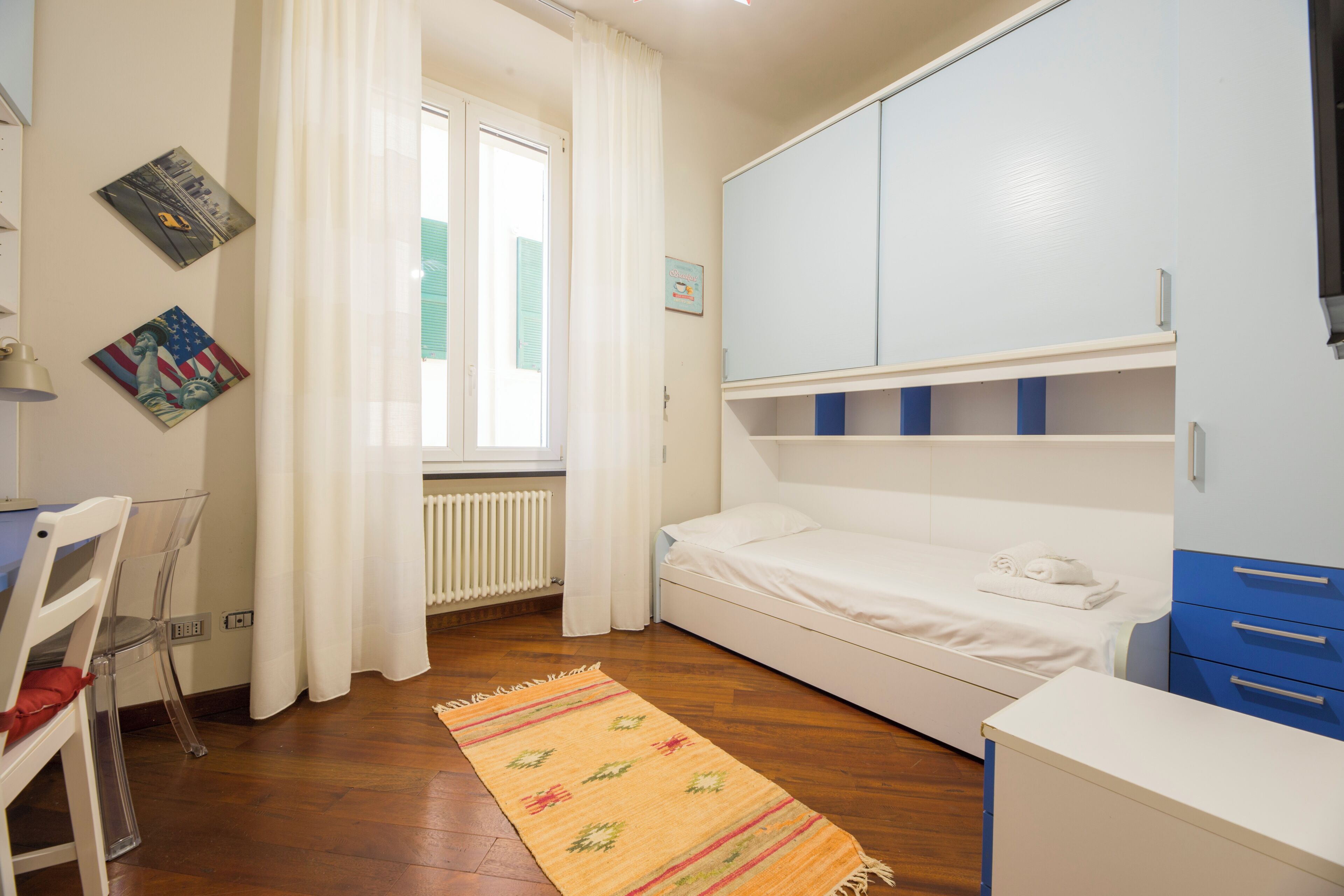 Une chambre à coucher comprenant un lit, un bureau, une chaise, un radiateur et une fenêtre avec des rideaux.