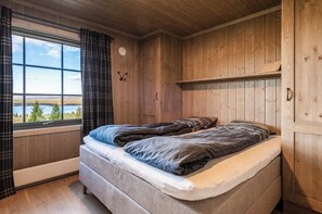 A wooden room with a bed, a window with curtains, and a view of the outdoors. - New cabin with views of Tisleiefjorden (Gol)