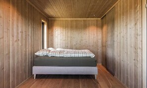 A small, wooden-paneled room with a single bed, a bench, and a door.