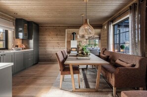 A modern kitchen with wooden walls, a dining table, and a sofa. - New cabin with views of Tisleiefjorden (Gol)
