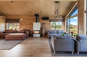A modern log cabin interior with a fireplace, two sofas, and large windows offering a view of the outdoors.