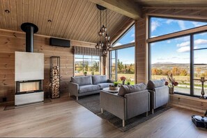 A modern living room with a fireplace, large windows, and a view of the outdoors. - New cabin with views of Tisleiefjorden (Gol)