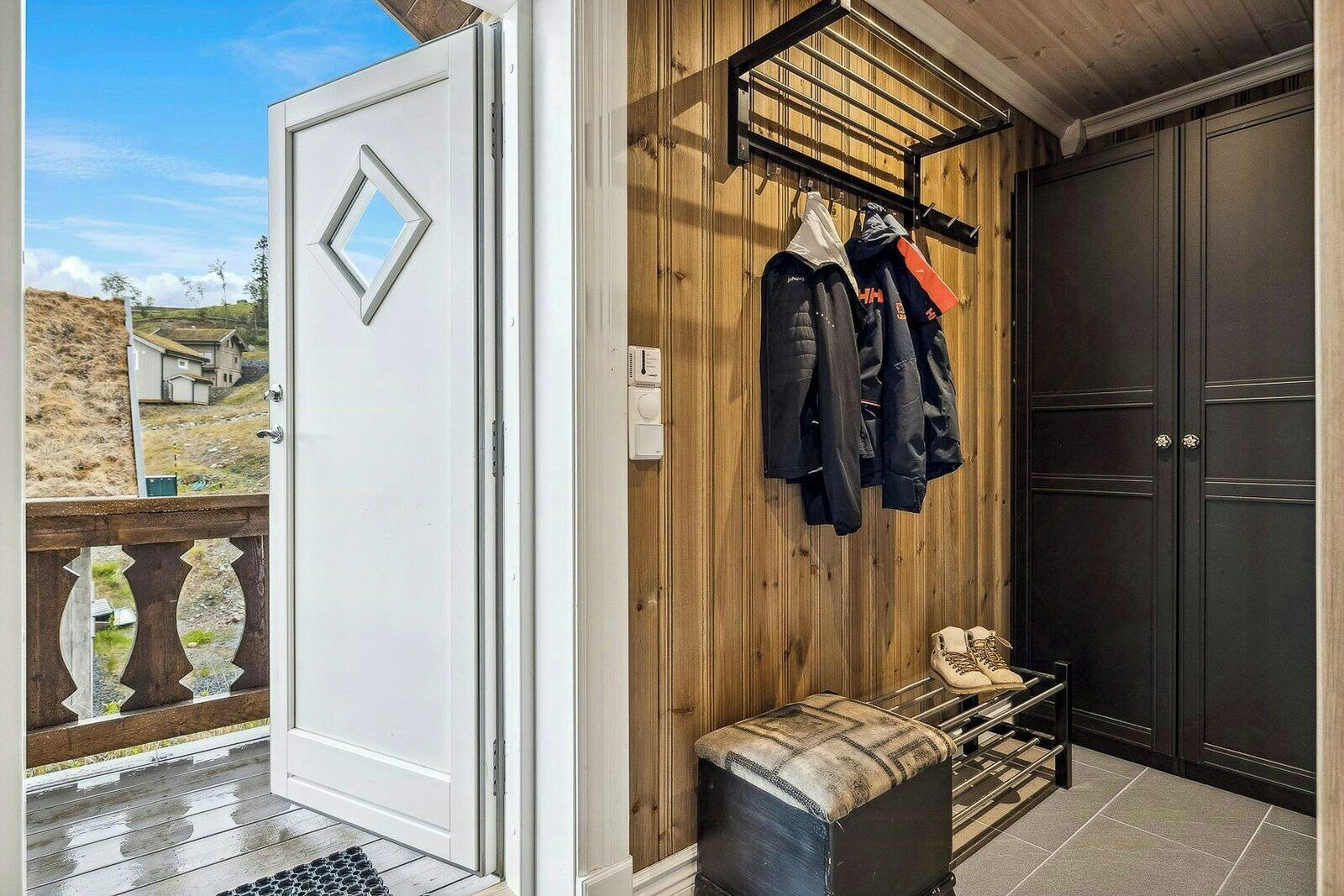 Een kamer met een houten wand, een kapstok met jassen, een bank en een deur.