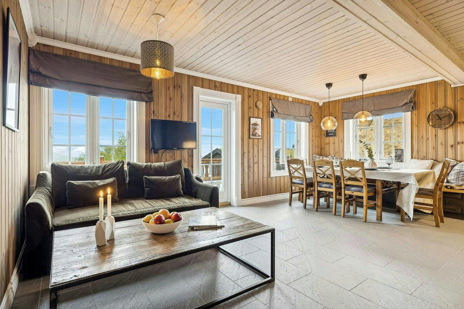 A cozy room with a sofa, dining table, and chairs, wooden walls, and a TV.