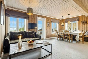 A cozy room with a sofa, dining table, and chairs, wooden walls, and a TV. - Ski-in/ski-out cabin in Holtardalen (Rauland)