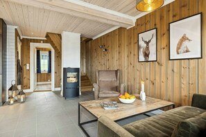 A cozy room with a fireplace, a sofa, a dining table with fruit, and framed wildlife pictures on the wall. - Ski-in/ski-out cabin in Holtardalen (Rauland)