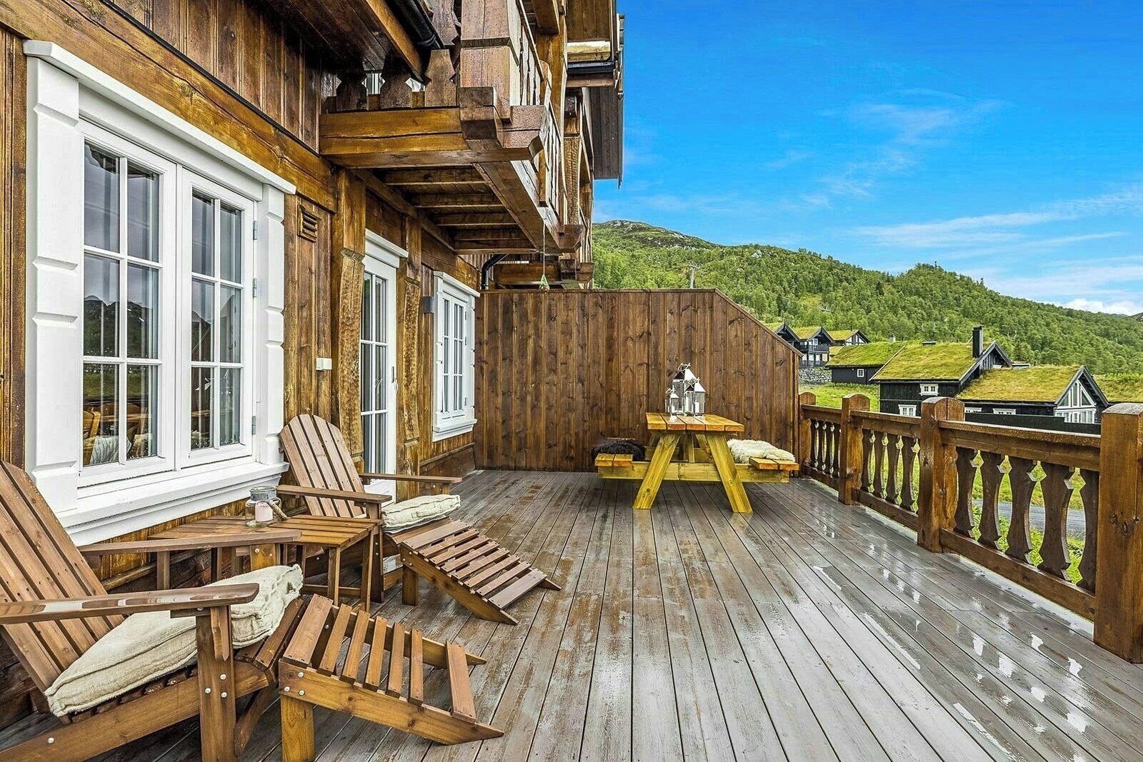 Una terraza de madera con sillas Adirondack y una mesa, con vistas a una ladera verde.