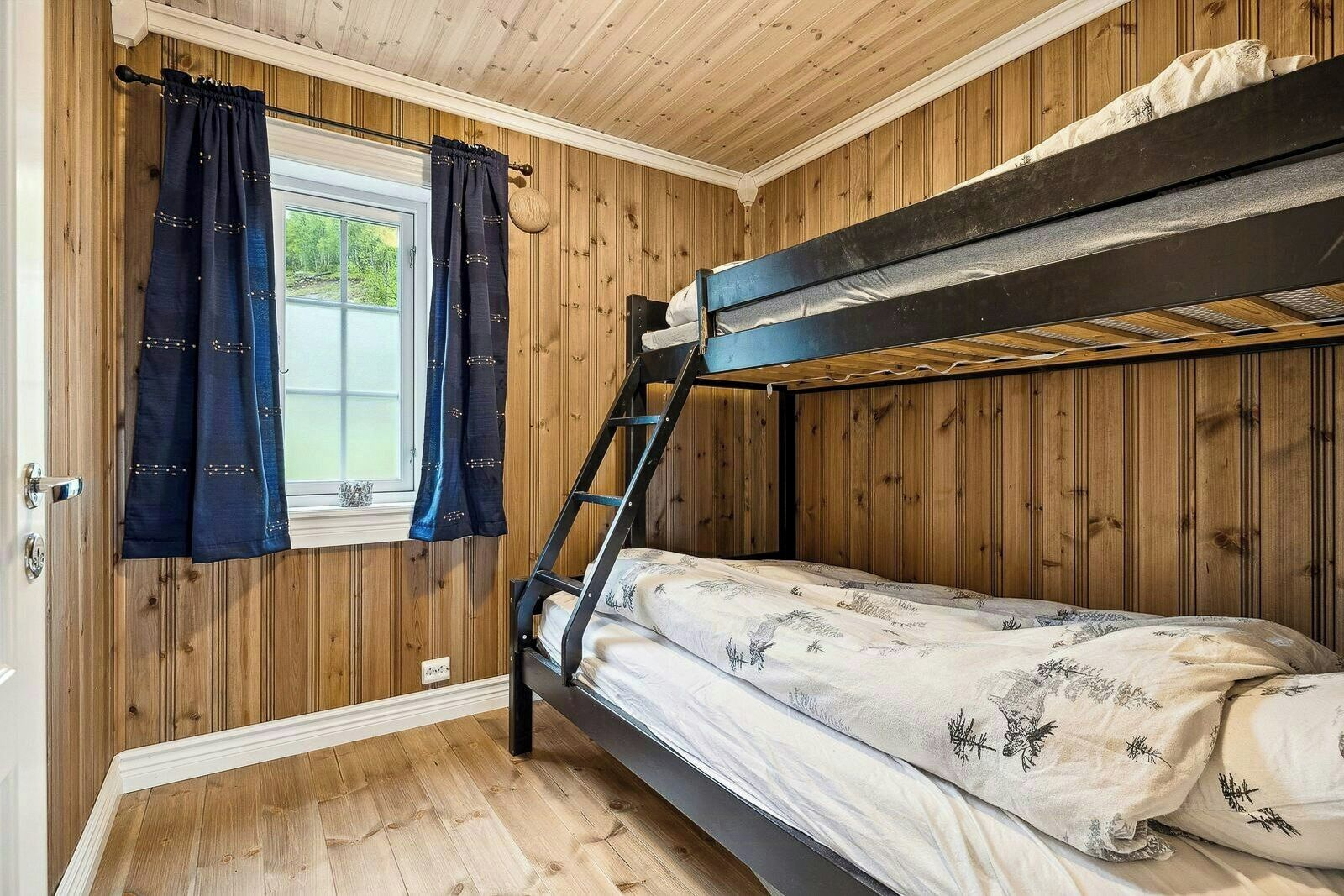 Ein Schlafraum mit Etagenbetten, Holzwänden, einem Fenster mit Vorhängen und einer Leiter.