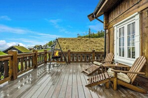 A wooden deck with outdoor seating, a grill, and a view of houses with grass roofs. - Ski-in/ski-out cabin in Holtardalen (Rauland)