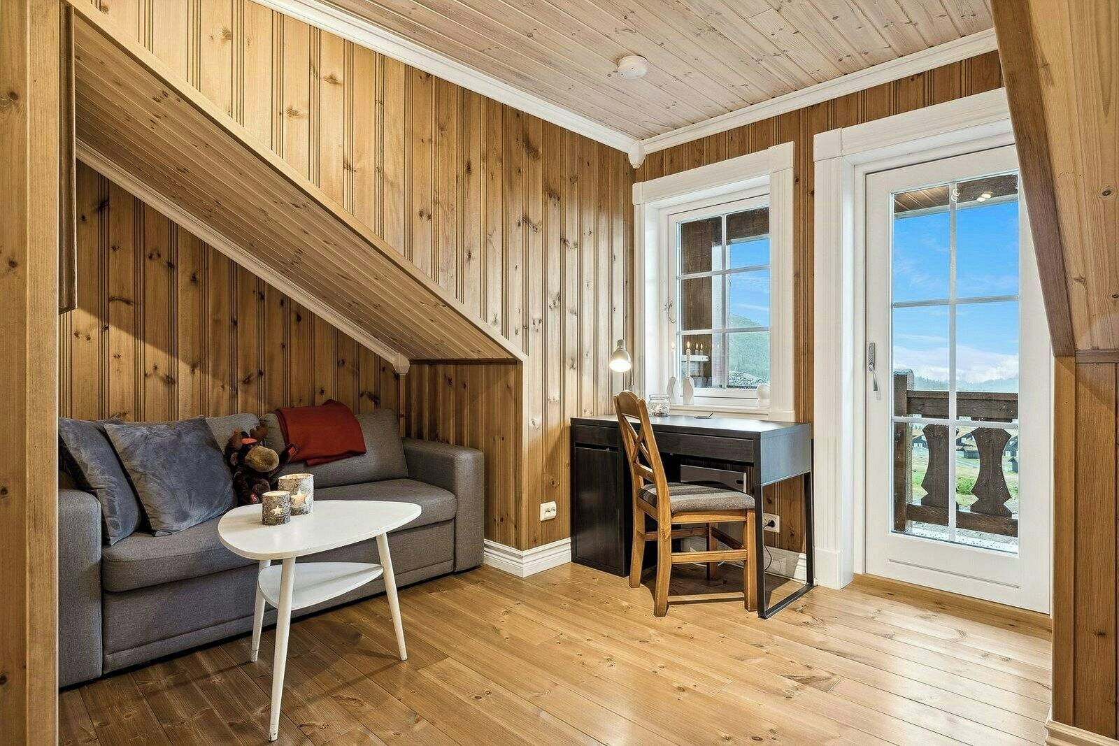 A room with wooden paneling, a sofa, a dining table with a chair, and a window with a view.