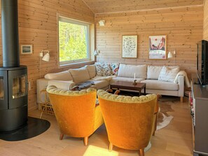 Ein gemütliches Blockhauss-Interieur mit einer Couch, zwei Sesseln, einem Couchtisch, einem Kamin und Kunstwerken an den Wänden.