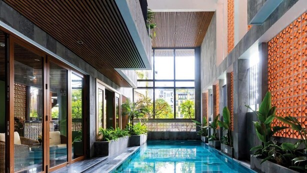 Una piscina interior moderna con puertas de vidrio, techo de madera y vistas a zonas verdes.