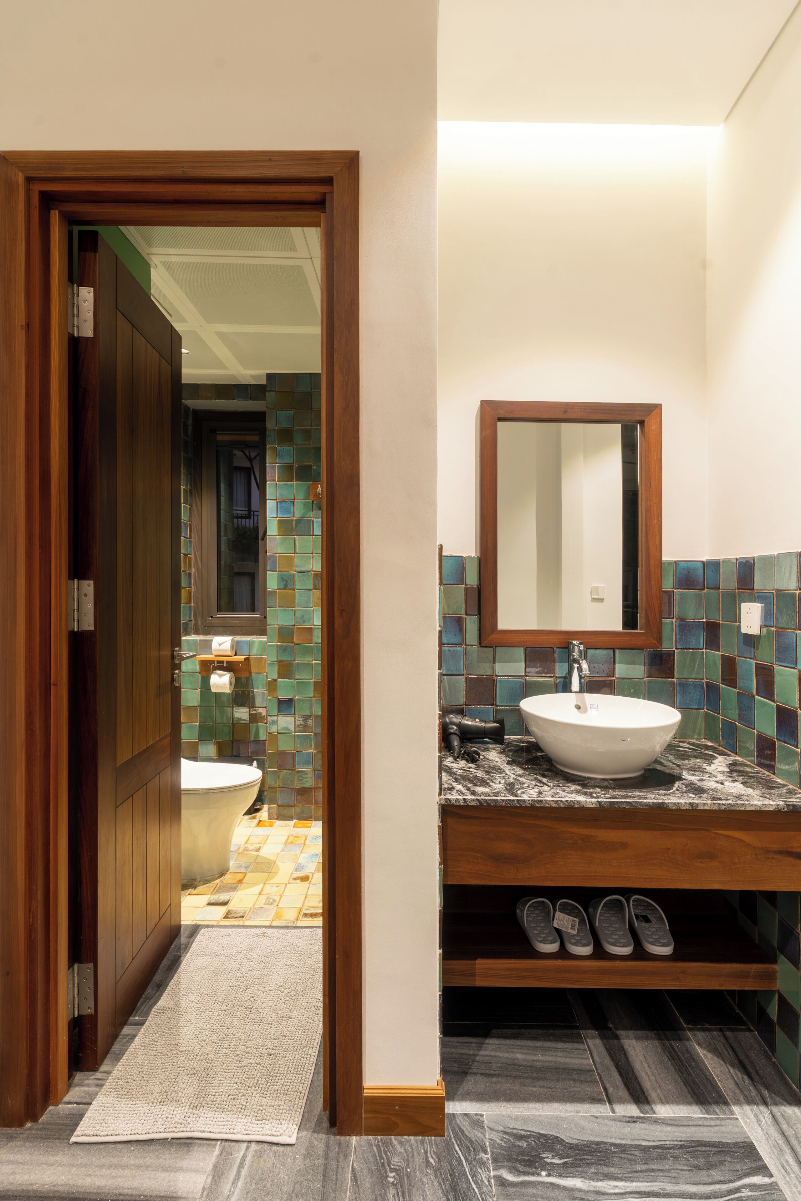 Une salle de bain avec un meuble-lavabo en bois, un évier, un miroir et un pare-feu en carreaux.