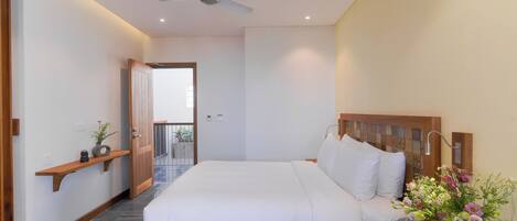 A modern hotel room with a large bed, a wooden headboard, a bedside table with a vase of flowers, and a ceiling fan.