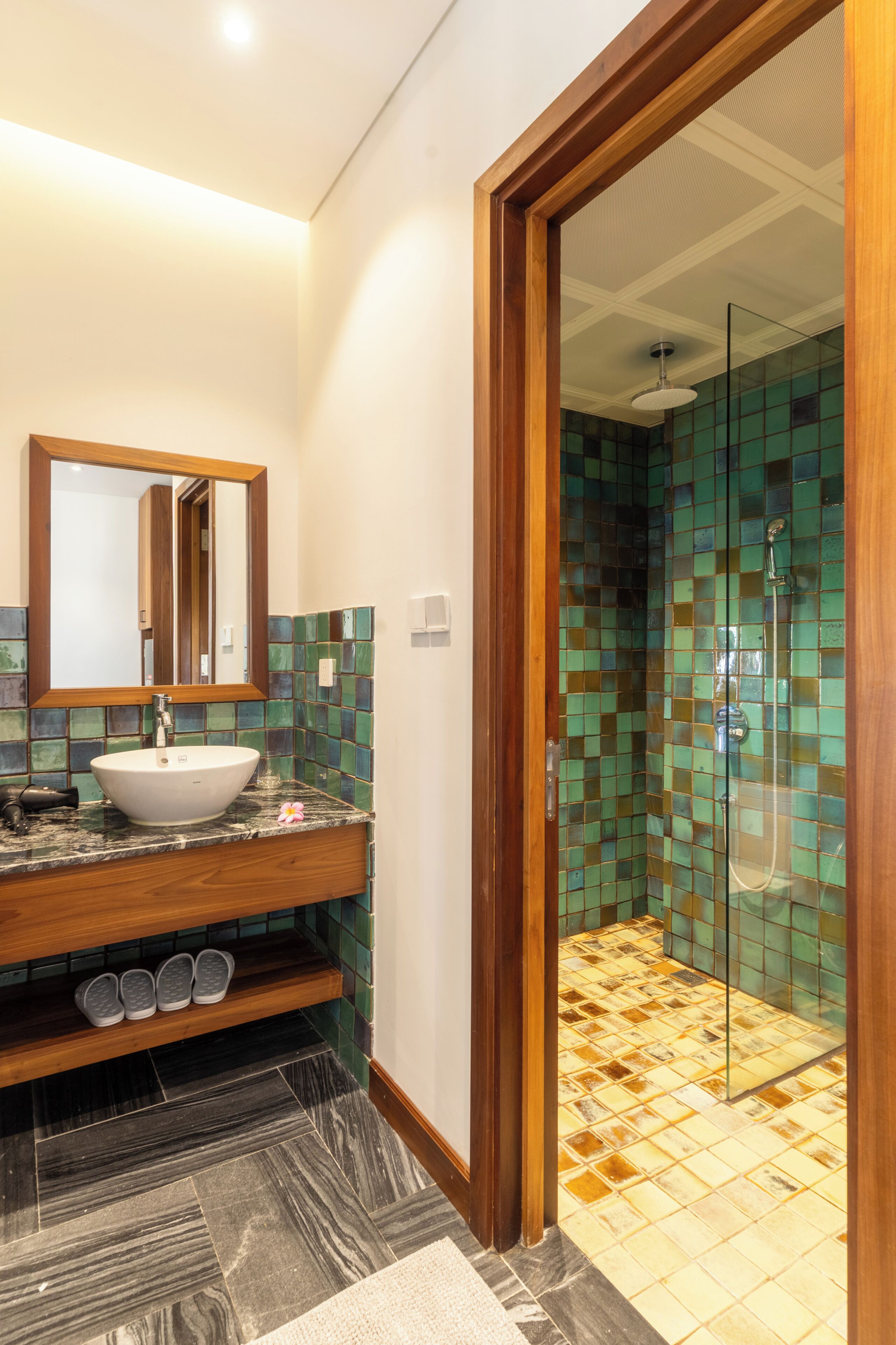A bathroom with a wooden vanity, a large mirror, and a shower with mosaic tiles.