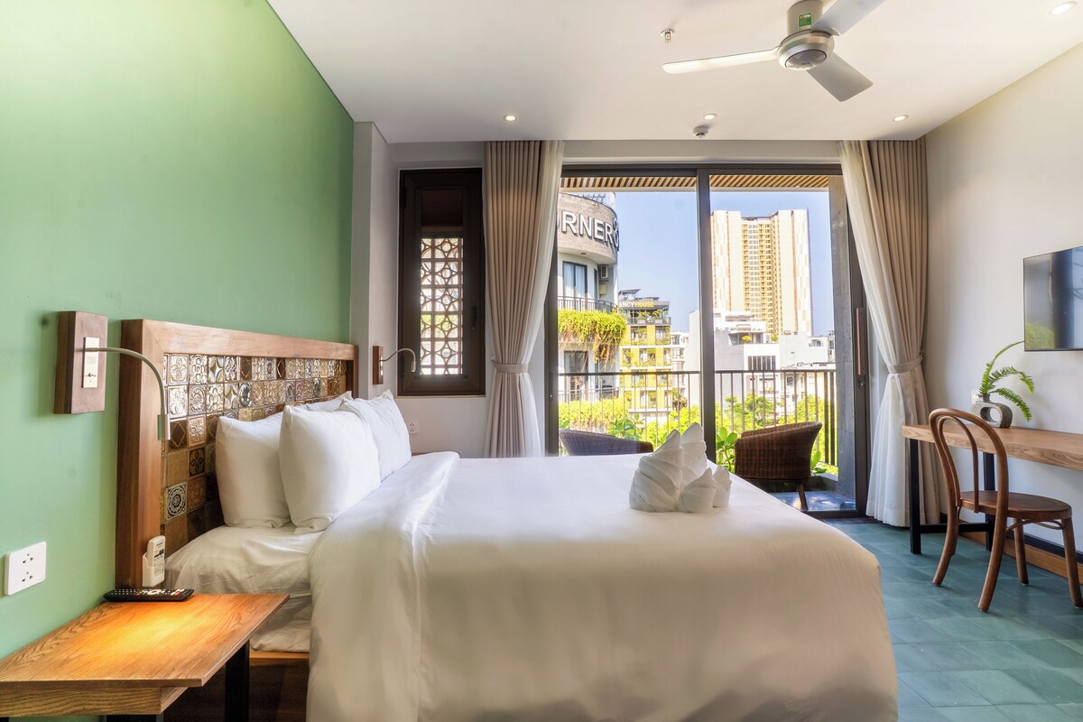 Une chambre d’hôtel comprenant un lit, un bureau, une chaise, une télévision et un balcon avec vue sur les immeubles.