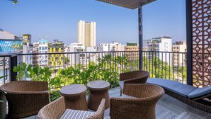 Un balcón con mobiliario de mimbre, vistas a edificios y cielo despejado.