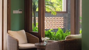 Una habitación con dos sillas de mimbre, una mesita y vistas al exterior con vegetación.