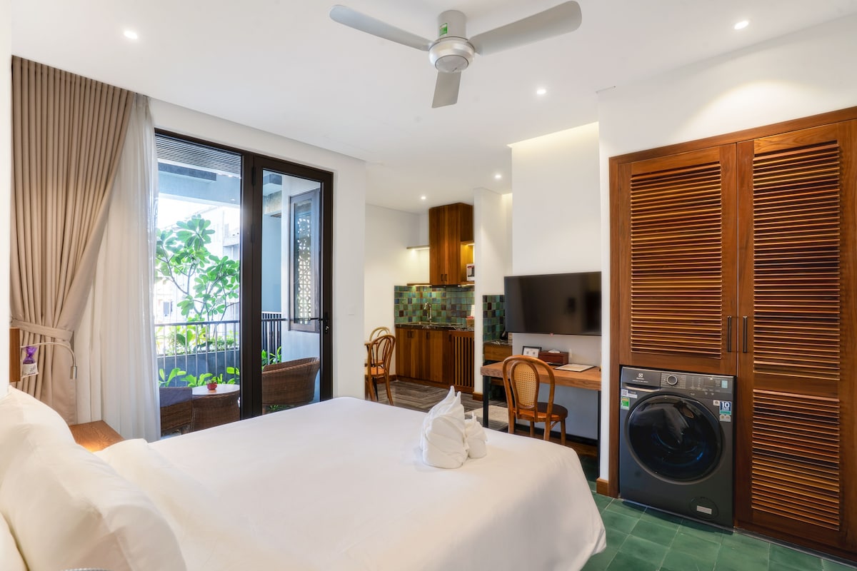 Quarto de hotel com cama, máquina de lavar, área de refeições e vista para o verde lá fora.