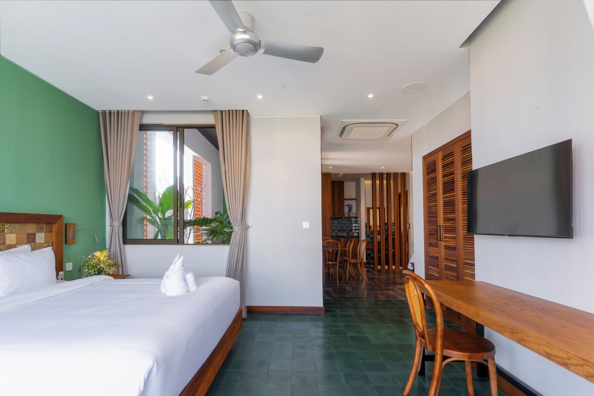 Une chambre d’hôtel équipée d’un lit, d’un bureau, d’une chaise, d’une télévision, d’un ventilateur de plafond et d’une fenêtre avec des rideaux.