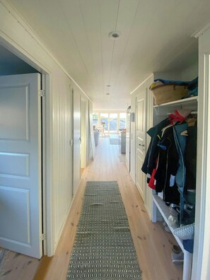 A narrow hallway with a wooden floor, a patterned rug, and a clothing rack on the right. - Seaside house with pool near Hällevikstrand (Ellös)