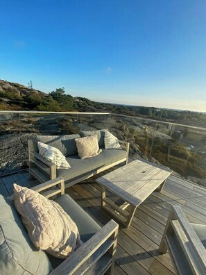 A wooden deck with a sofa and chairs, overlooking a rocky landscape. - Seaside house with pool near Hällevikstrand (Ellös)