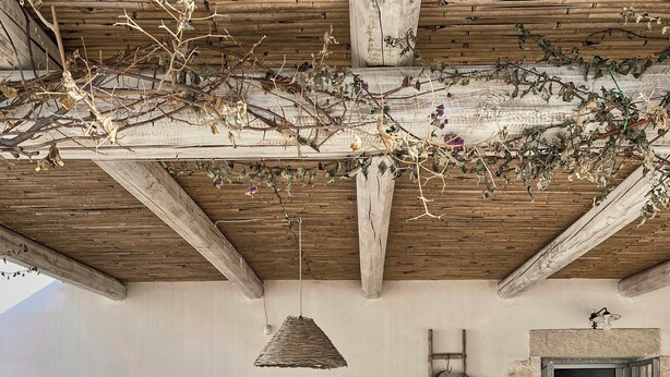 Un espace de restauration extérieur de style rustique, avec un sol carrelé en pierre, des chaises en bois, une nappe à motifs et un luminaire suspendu.