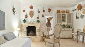 Une pièce avec une cheminée en pierre, un lit, une chaise, une table à manger et un coin cuisine équipé de placards et de casseroles suspendues.
