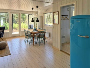 Een eetgedeelte met een houten tafel en stoelen, een blauwe koelkast en grote ramen.