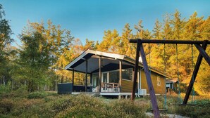 Une cabane dotée d’un porche abrité, d’une balançoire et entourée d’une forêt.