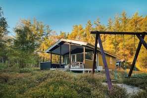 Een blokhut met een overdekte veranda, een schommel en een bebost landschap op de achtergrond.