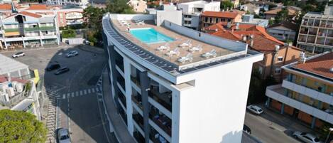 Un edificio de varios pisos con piscina en la azotea y tumbonas.