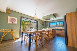 A modern kitchen with a dining table, chairs, pendant lights, and a view of the outdoors. - Luxury villa with pool in Baho (Baho)