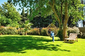 A person sitting on a swing chair in a lush garden with a bench nearby. - Luxury villa with pool in Baho (Baho)
